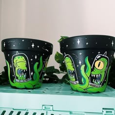 two plant pots with green monster designs on them sitting on a shelf next to plants