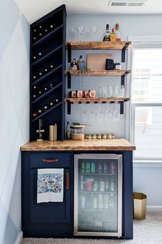 a small bar with wine glasses and bottles on the top shelf, next to a mini fridge