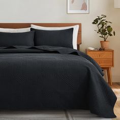 a bed with black bedspread and pillows in a room next to a plant