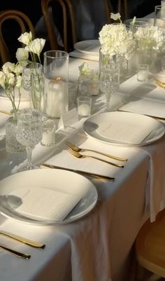 the table is set with white flowers and place settings