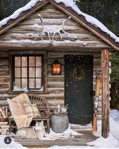 a small log cabin in the snow with two dogs laying on it's front porch