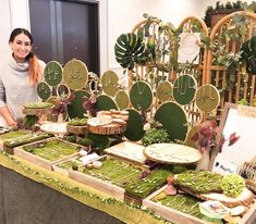 a woman standing in front of a table filled with cakes and pies on top of green trays