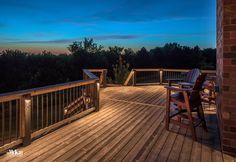 a wooden deck with two chairs on it at night, overlooking the trees and sky