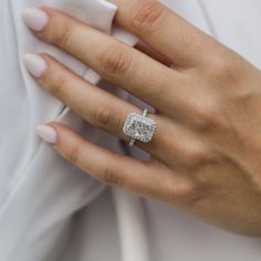 a woman's hand with a diamond ring on her left hand, wearing a white shirt