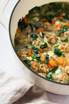 a pot filled with meatballs and vegetables on top of a white table cloth next to a napkin