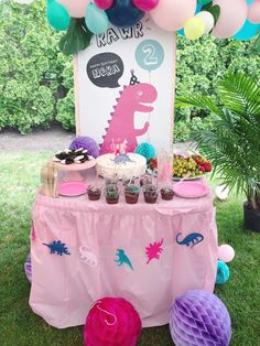 a pink table topped with cake and cupcakes on top of a lush green field