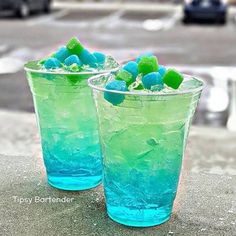 two glasses filled with blue and green liquid on top of a cement slab next to a street