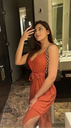 a woman in an orange dress taking a selfie with her cell phone while standing next to a bathroom sink