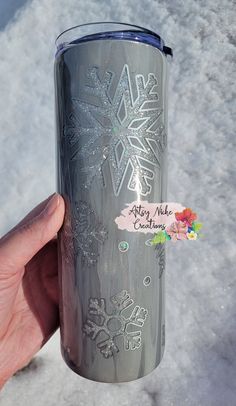 a person holding up a silver tumbler with snowflakes on it in the snow