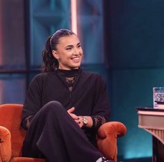 a smiling woman sitting in an orange chair on the set of tv talk with host