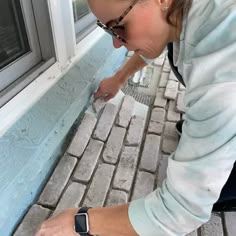 a woman is painting the side of a brick building with blue paint and white trim