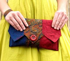 a woman in a yellow dress is holding a red and blue purse with a button on it