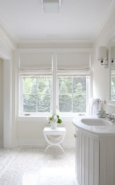 a white bathroom with two windows and a sink