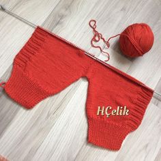 a red knitted baby's pants with the word hello written on it next to a ball of yarn