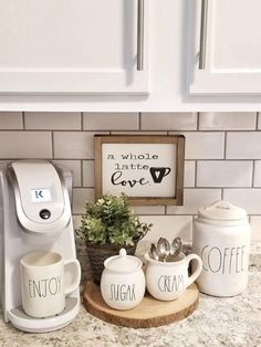 coffee maker, cups and mugs are on the counter in front of white cabinets