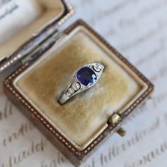 an antique ring with a blue stone sits in a box on top of a piece of paper