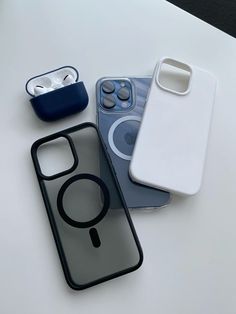 three cell phones are sitting on a white table with ear buds and an iphone case