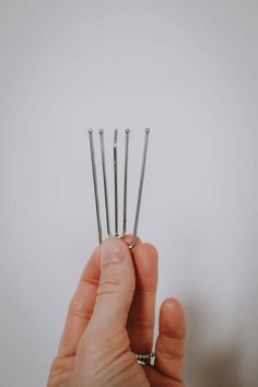 a hand holding several small pins in it's left side, with the top one being held up