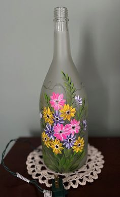 a painted glass bottle sitting on top of a doily next to a charger