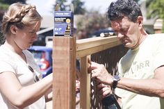 a man and woman are working on a wooden fence