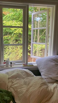 an unmade bed in front of two windows with trees outside the window sill