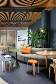 an office with blue carpet and wooden ceilinging, round tables and chairs in front of the couches