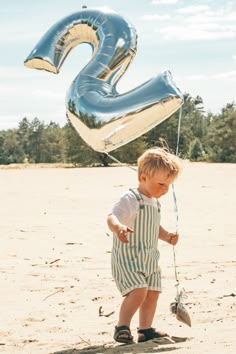 a little boy standing on top of a sandy beach next to a number 2 balloon