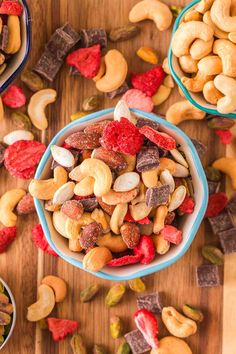 two bowls filled with mixed nuts on top of a wooden table next to other snacks