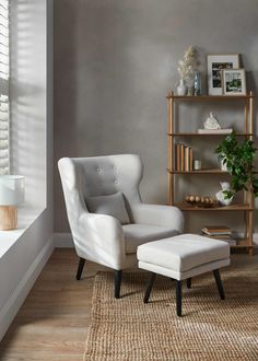 a white chair and ottoman in a room with wooden flooring, gray walls and windows