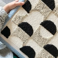 someone is holding up a black and white rug with squares on the bottom, which have been crocheted