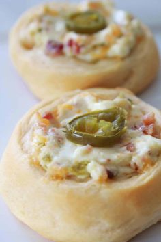 two mini pizzas with cheese and jalapenos in them on a white surface