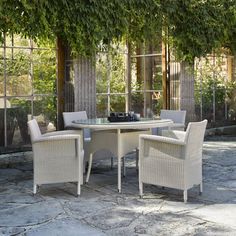 an outdoor dining table and chairs with ivy growing on the wall behind it, surrounded by stone patio tiles