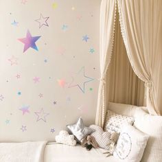 a white bed sitting under a window next to a wall with colorful stars on it