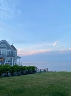 a large house sitting on top of a lush green field next to the ocean at dusk