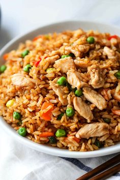 a white bowl filled with chicken and rice next to chopsticks on a table