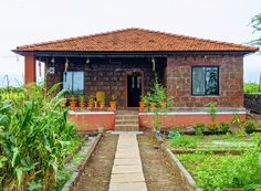 a small brick house sitting in the middle of a lush green field with lots of plants