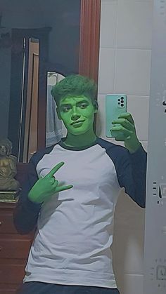 a man with green paint on his face is taking a selfie in front of a mirror