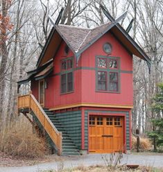 a red and green house in the woods with stairs leading up to it's second story