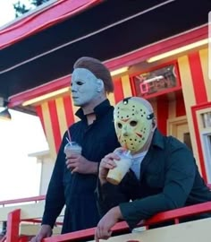 two people wearing masks standing in front of a red and yellow striped building with drinks