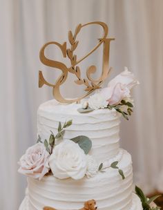 a wedding cake with white frosting and flowers on the top, topped with a gold monogram