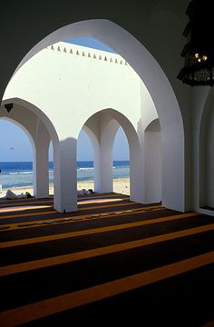 the interior of an empty church with arches and striped carpet on the floor, looking out at the ocean