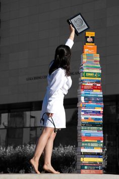 a woman standing on top of a pile of books next to a tall stack of books