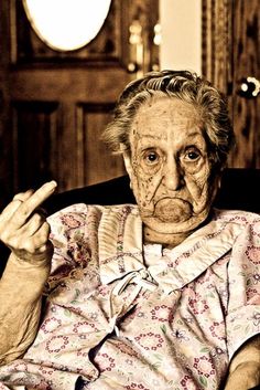 an old woman sitting in a chair with her hand up to the side and pointing at something