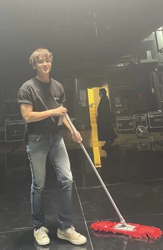 a young man is cleaning the floor with a mop and duster in front of him