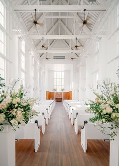 an aisle with white chairs and flowers in vases on each side, along with wooden flooring