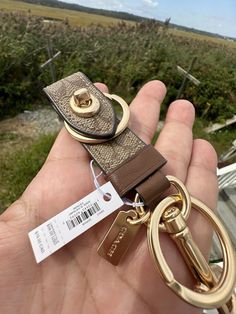 a hand holding a keychain with a tag attached to it, in front of a field