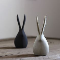 two small white and black vases sitting on top of a wooden table next to each other