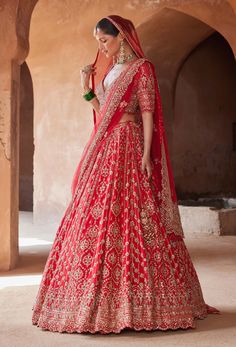 a woman in a red and gold lehenga with her hand on her hip