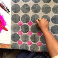 a person is painting on a piece of fabric with pink and black circles in the background