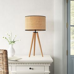 a white table with a lamp on it and a wicker basket next to it